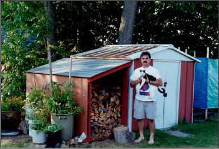 Ernie Bies stand by tin shed, holding black and white cat.